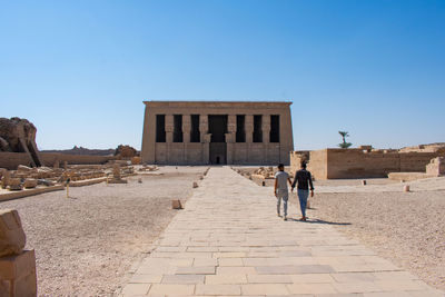 Rear view of people walking on street against clear blue sky