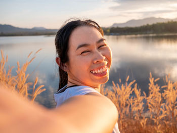 Portrait of beautiful asian woman smiling and looking to camera at sunset lakeside.