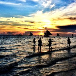 Silhouette people on beach against sky during sunset