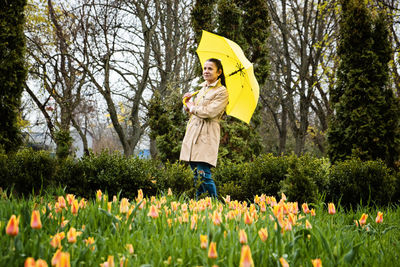 Happy senior woman in yellow rain coat with yellow umbrella walking in park. cheerful mature