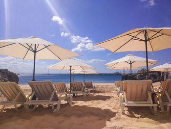 Deck chairs and parasols on beach against sky