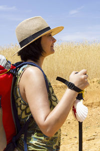 Side view of hiker in hat with backpack standing on hill during sunny day