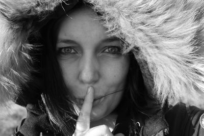 Close-up portrait of woman wearing warm clothing with finger on lips