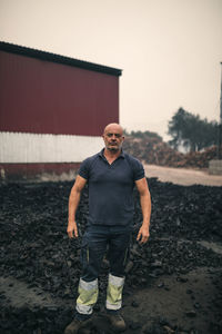 Worker standing in front of coal heap at factory