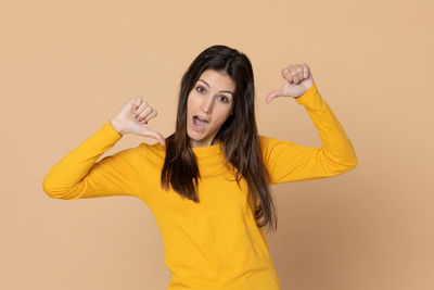 Portrait of young woman standing against yellow background