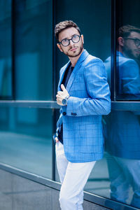 Portrait of handsome young man standing by glass building