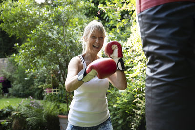 Cheerful senior woman punching punch bag while standing in back yard on sunny day