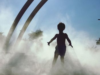 Silhouette boy standing amidst smoke against clear blue sky