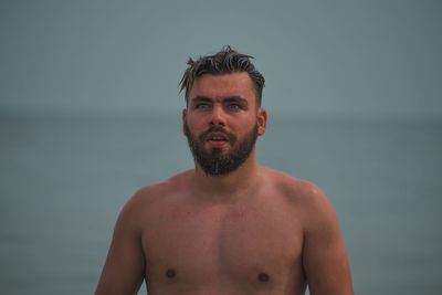 Portrait of shirtless man standing against water