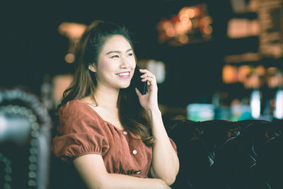 Smiling woman using mobile phone while sitting on sofa