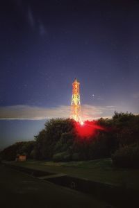 Low angle view of illuminated communication tower on hill against sky