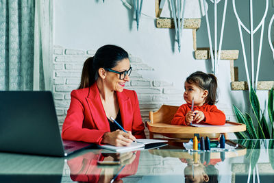 Young executive woman working from home while taking care of her young daughter