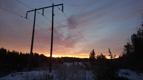 Silhouette trees on snow covered landscape against sky during sunset