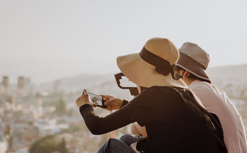 Rear view of man with woman sitting against sky in city