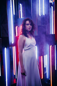Portrait of young woman standing against illuminated room
