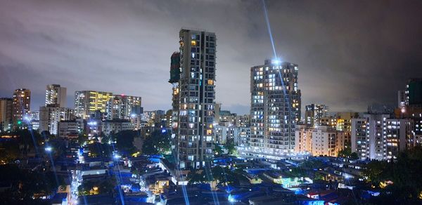 Illuminated modern buildings in city against sky at night