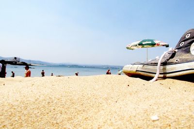 Cropped image of shoe at beach against clear sky on sunny day