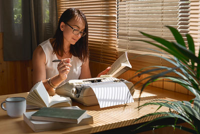 Female writer in glasses looking for inspiration to start a new novel on her retro writing machine.