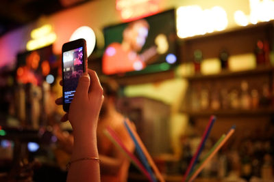 Cropped hand of woman using mobile phone while sitting in bar at night