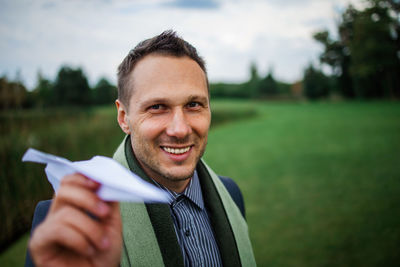 Happy businessman holding paper plane in green field