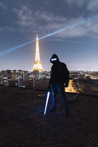 Rear view of man standing against illuminated buildings in city