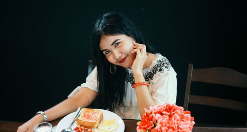 Portrait of smiling woman with breakfast on table sitting against black background