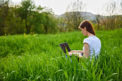 Young woman using mobile phone while sitting on field