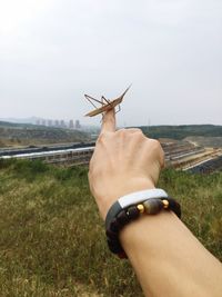 Close-up of man hand on field against sky