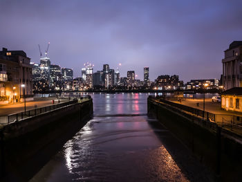 Illuminated buildings by river against sky in city at night