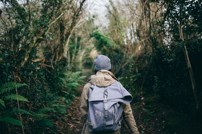 Rear view of woman walking on pathway amidst trees at forest