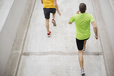 Rear view of male athletes running on footpath at parking lot