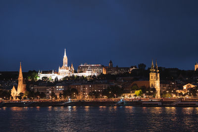Illuminated buildings by river against sky at night