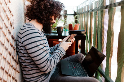 Side view of man using mobile phone while sitting in balcony