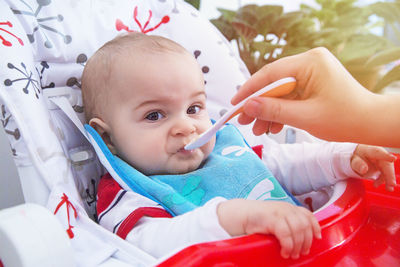 Cropped hand of mother feeding baby boy sitting in stroller