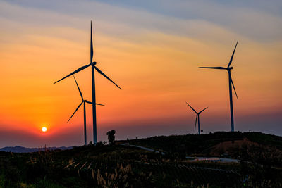 Silhouette wind turbines on land against sky during sunset