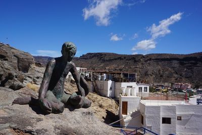 Statue by buildings against blue sky