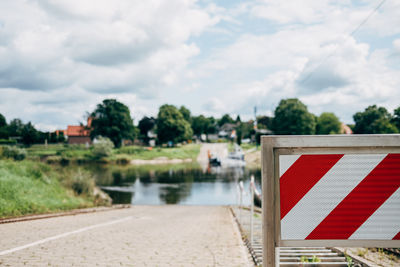 Road sign by lake against sky