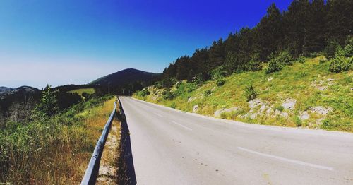 Empty road leading towards mountains against clear sky