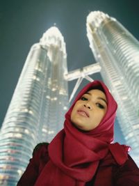 Portrait of woman against illuminated petronas towers in city at night