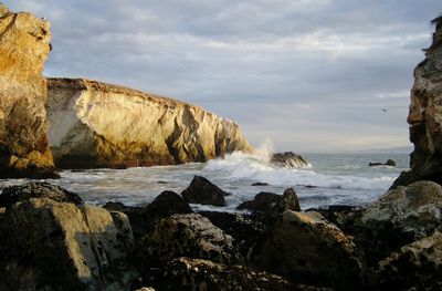 Rock formations in sea against cloudy sky