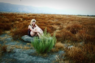 Portrait of young woman sitting on wood at field