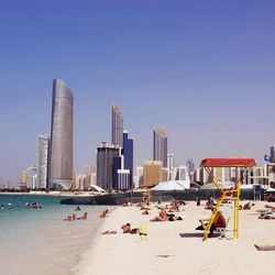 People relaxing at beach by city against sky