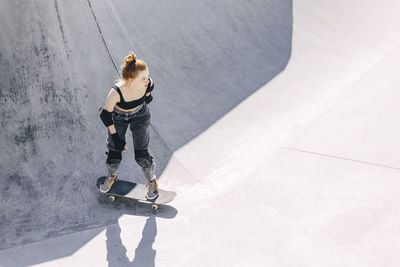 Contemplative teenager standing on skateboard at sunny day