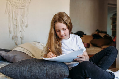 The girl after school plays at home, draws with pencils and felt-tip pens