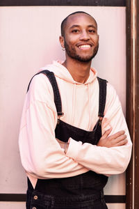 Portrait of smiling young man standing with arms crossed against wall