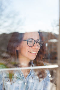 Smiling woman wearing eyeglasses seen through glass window