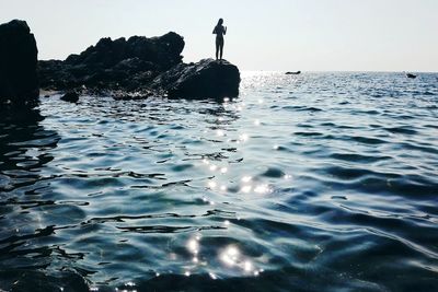 Man on rock in sea against sky