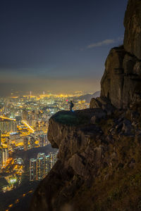 Person at illuminated city against sky during sunset