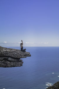 Man on rock by sea against clear blue sky