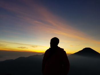 Silhouette mid adult man standing on mountain against sky during sunset